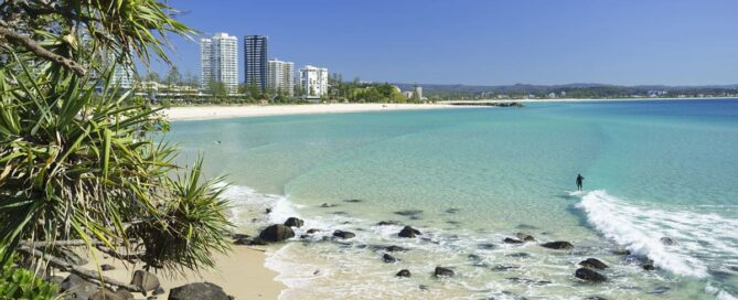 Coolangatta Beach with clear blue water, sandy shoreline and high-rise buildings in the distance.