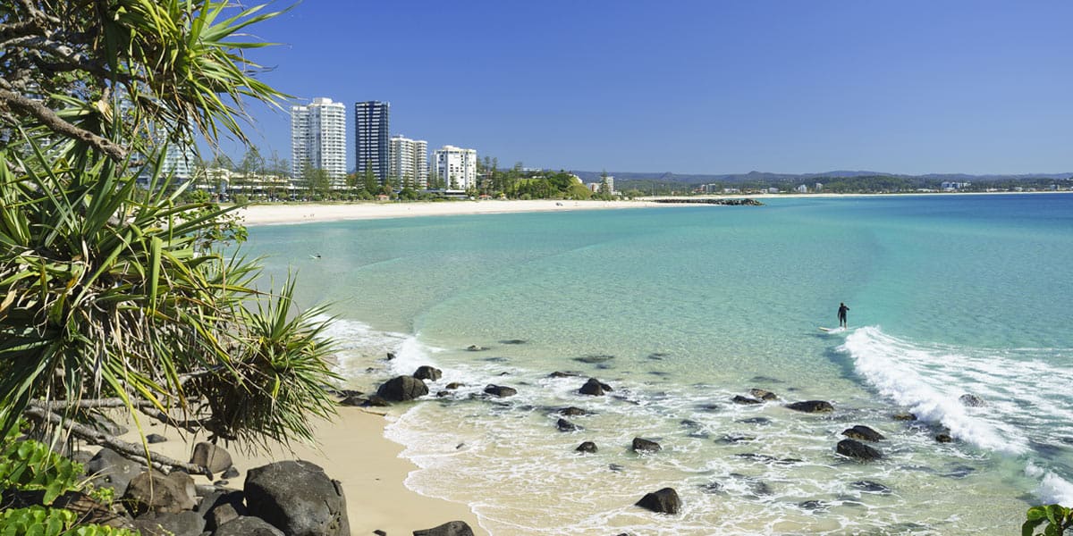 Coolangatta Beach with clear blue water, sandy shoreline and high-rise buildings in the distance.
